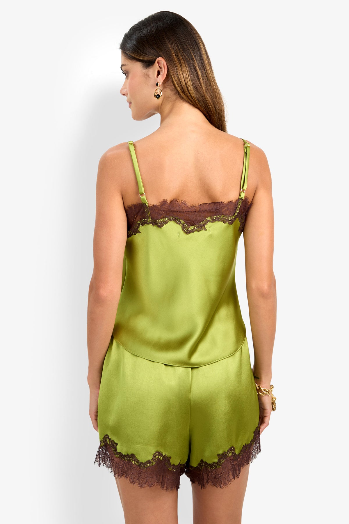 A woman is shown from the back against a plain white background, wearing the Amoira Top—a green satin camisole with brown lace trim—paired with matching shorts.