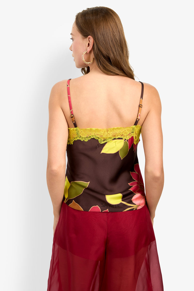 A woman with brown hair is shown from the back, wearing the Amoira Top—a floral camisole with yellow lace—and red sheer pants.