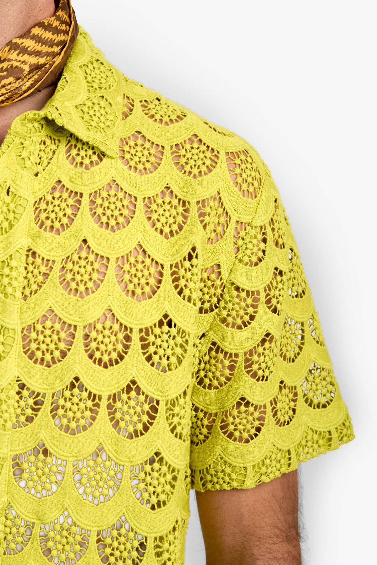 A person wearing the Branson Shirt—a yellow, scallop-patterned crochet top with a pointed collar—paired with a brown patterned scarf around the neck. Only the upper torso and part of the arm are visible against a white background.
