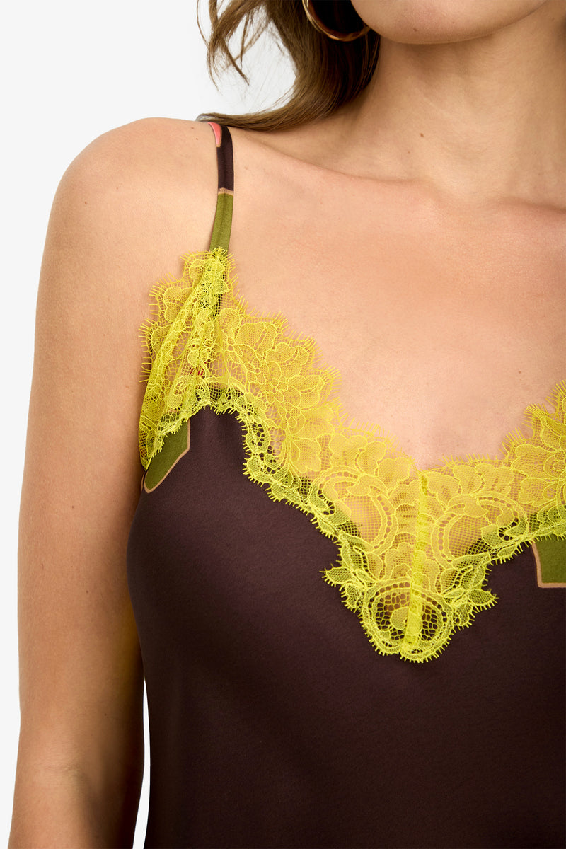 A woman wearing the CARAMIA DRESS (1), a brown camisole-style dress with thin straps and yellow lace trim along the neckline. Only her shoulder, chest, and part of her face are visible.