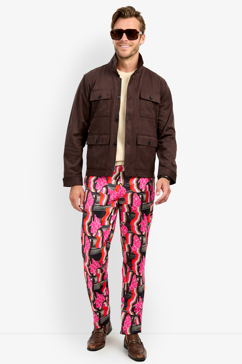 A man wearing sunglasses, a beige shirt, colorful patterned pink and black pants, brown shoes, and the HIGHLAND PARK JACKET stands smiling against a plain white background.