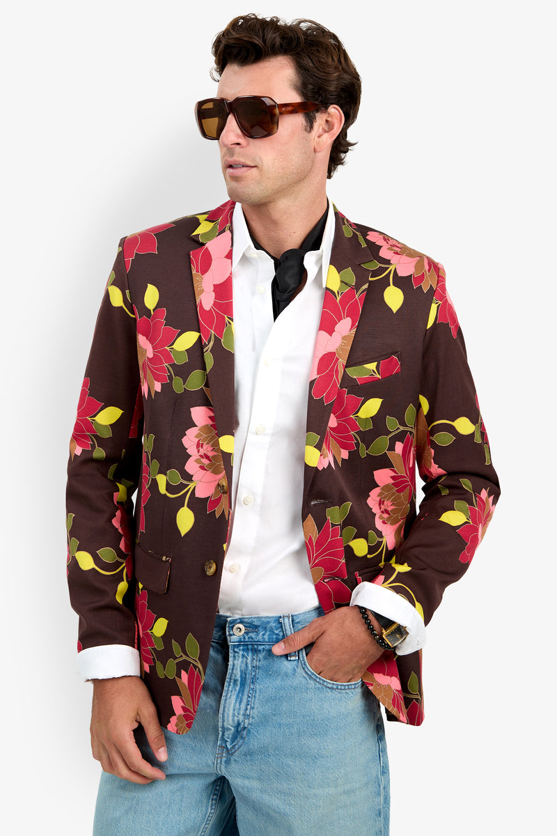 A man in sunglasses wears the Thurston Blazer—a brown floral jacket—over a white shirt and light blue jeans, standing with one hand in his pocket against a plain background.