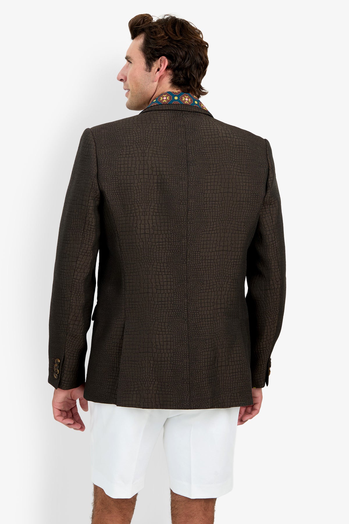A man facing away, wearing the Dohney Blazer—featuring a dark textured finish with embroidered collar detail—paired with white shorts, standing against a plain white background.