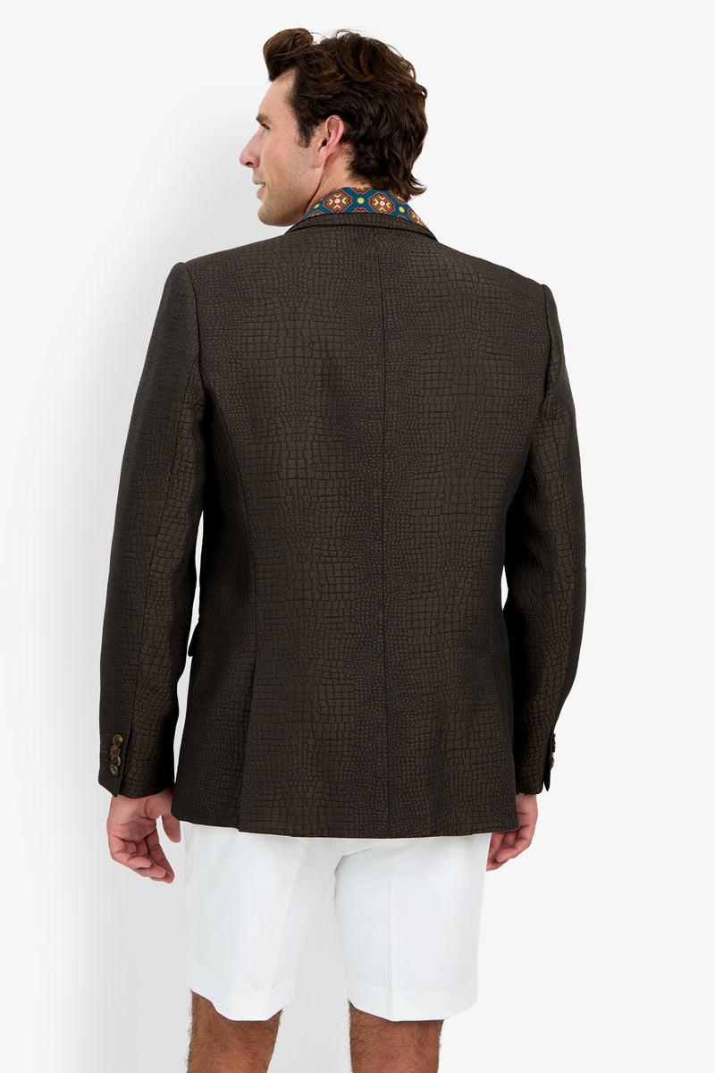 A man facing away, wearing the Dohney Blazer—featuring a dark textured finish with embroidered collar detail—paired with white shorts, standing against a plain white background.