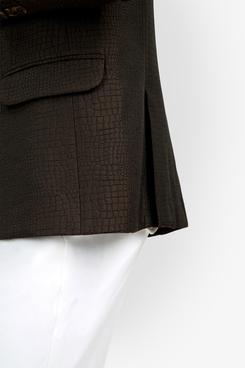 A close-up of a person wearing the Dohney Blazer, featuring a textured dark brown crocodile pattern, paired with white pants and shown from the waist down against a white background.