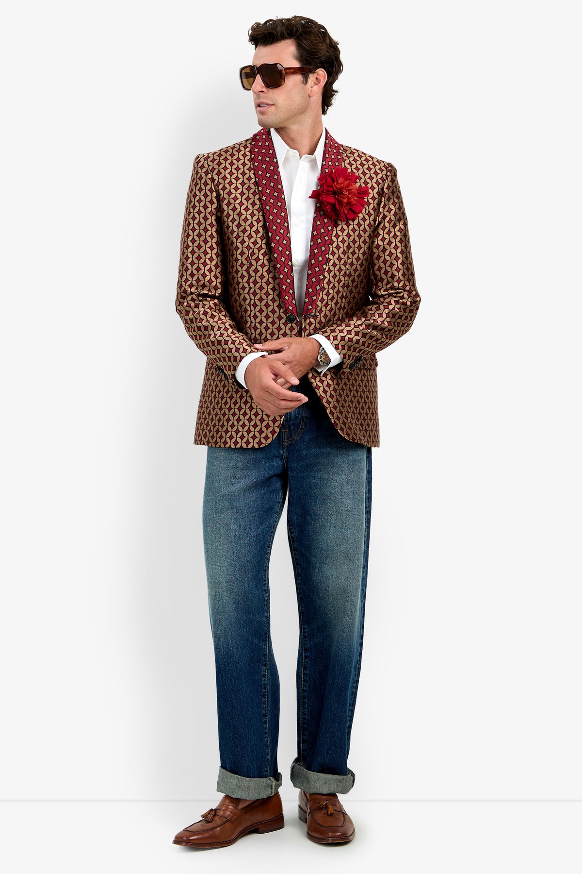 Man in the Alfred Blazer—a patterned blazer with a red lapel and flower pin—paired with a white shirt, sunglasses, rolled-up blue jeans, and brown dress shoes, standing against a white background.