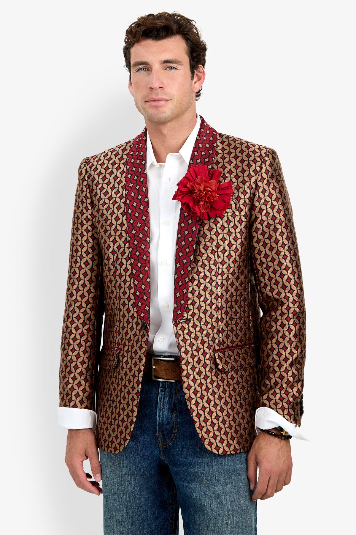 A man wearing the Alfred Blazer—a patterned gold and red jacket featuring a large red flower on the lapel—paired with a white dress shirt, blue jeans, and a brown belt, stands against a plain white background.