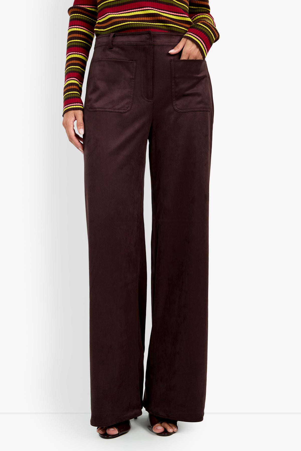 A person wearing the Zinn Pant—high-waisted, wide-leg dark brown pants with large front pockets—paired with a striped long-sleeve top, standing against a white background.