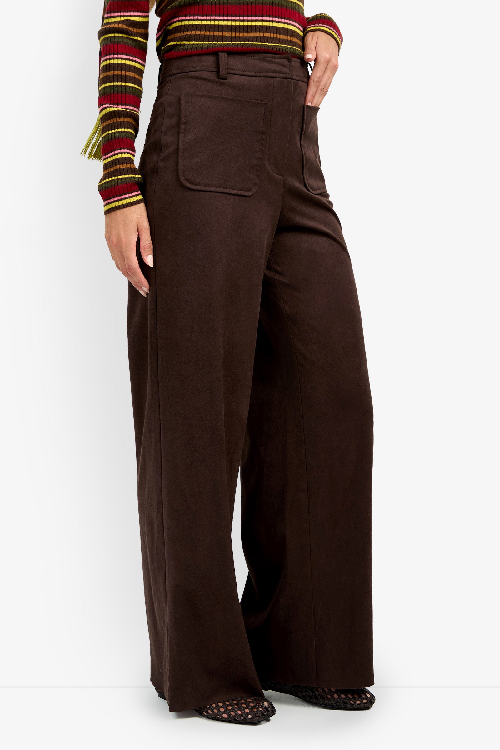 A person wearing the ZINN PANT—high-waisted, wide-leg brown pants with a front pocket—paired with a striped long-sleeve top and black woven shoes.