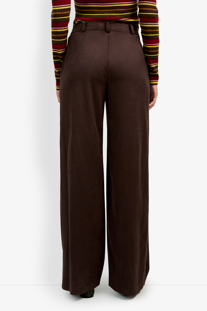 Wearing the ZINN PANT, high-waisted and wide-leg in brown, paired with a striped long-sleeve shirt, the person is shown from the back.
