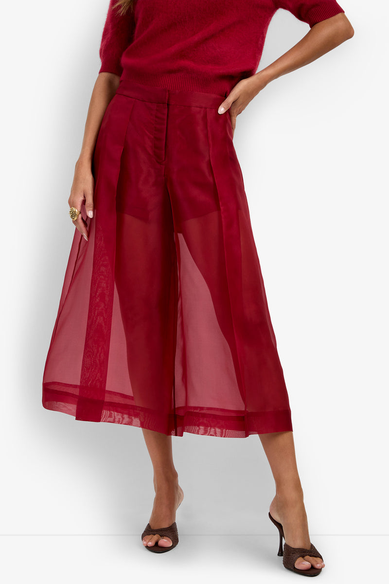 A person wearing the Siena Pant, a pair of sheer red wide-leg culotte pants with panels, and a red short-sleeve top, styled with heeled sandals against a white background.