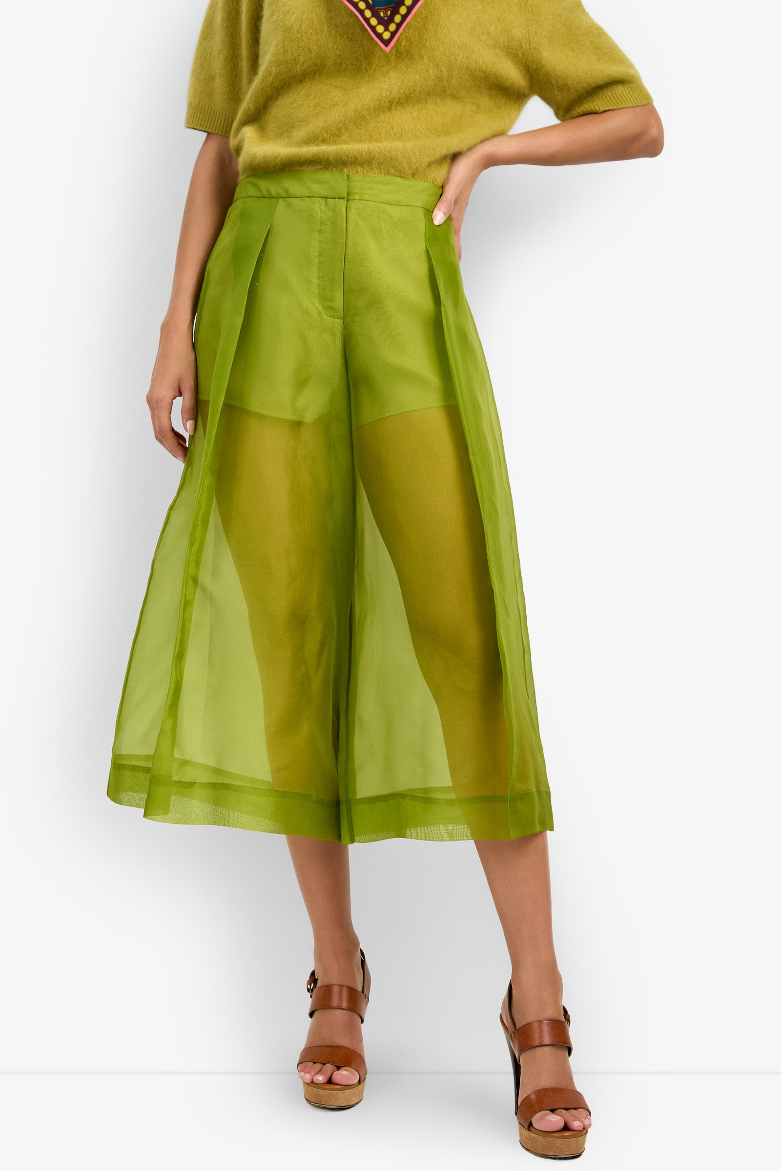 A person wearing the Siena Pant in sheer green, paired with a light green short-sleeve top and brown platform sandals, standing against a white background.