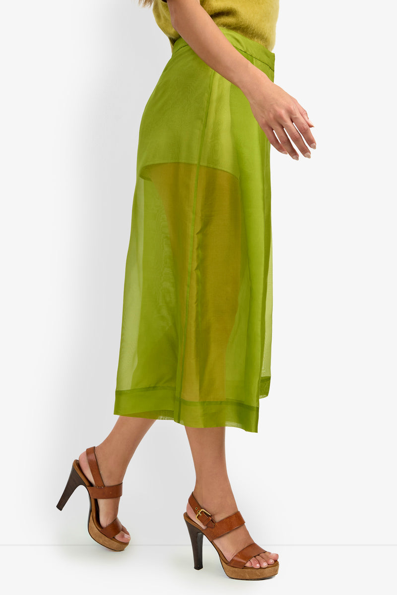 Woman wearing the SIENA PANT in sheer green, paired with a yellow-green top and brown high-heeled sandals, walking against a white background.