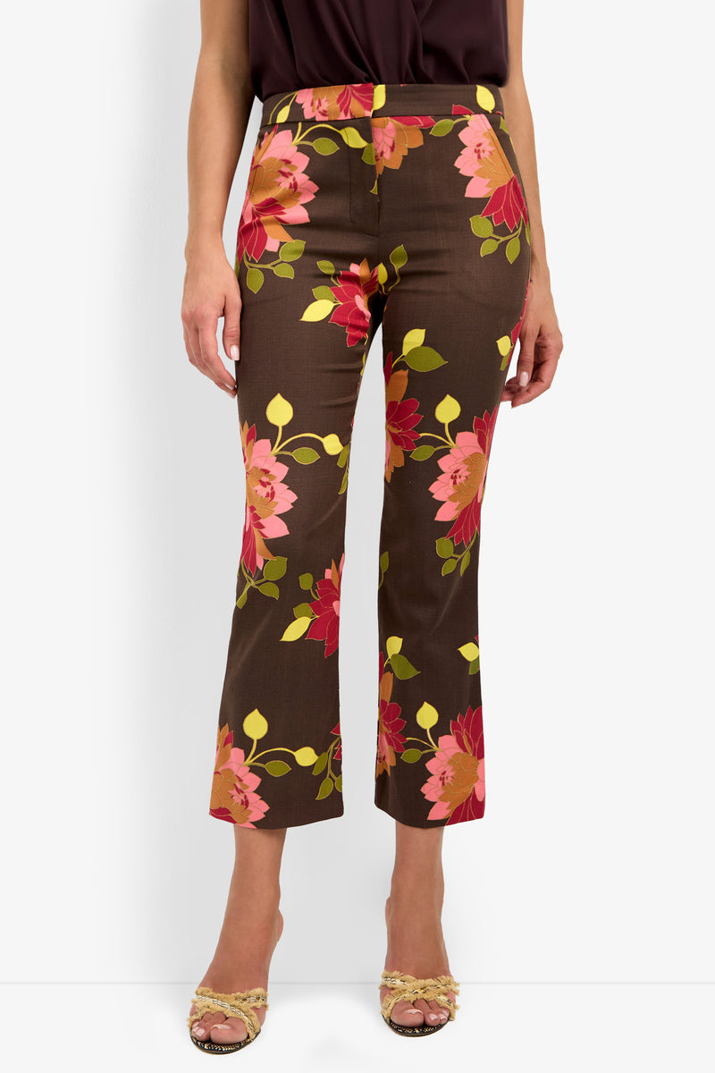 Wearing the LULU PANT, which features a pink and red floral print on a brown background, styled with a dark top and open-toe heeled sandals.