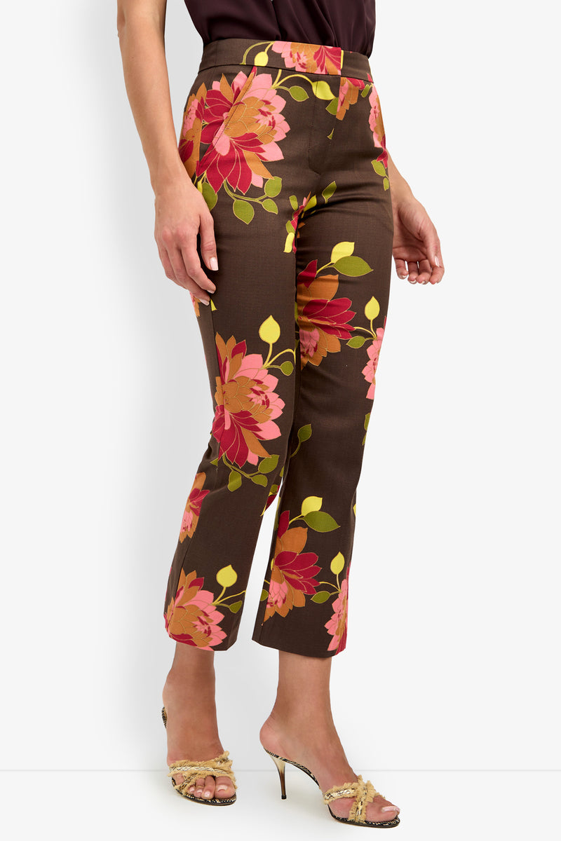 Wearing the LULU PANT—a pair of brown cropped pants featuring bold pink and orange floral prints—styled with open-toed high heel sandals.