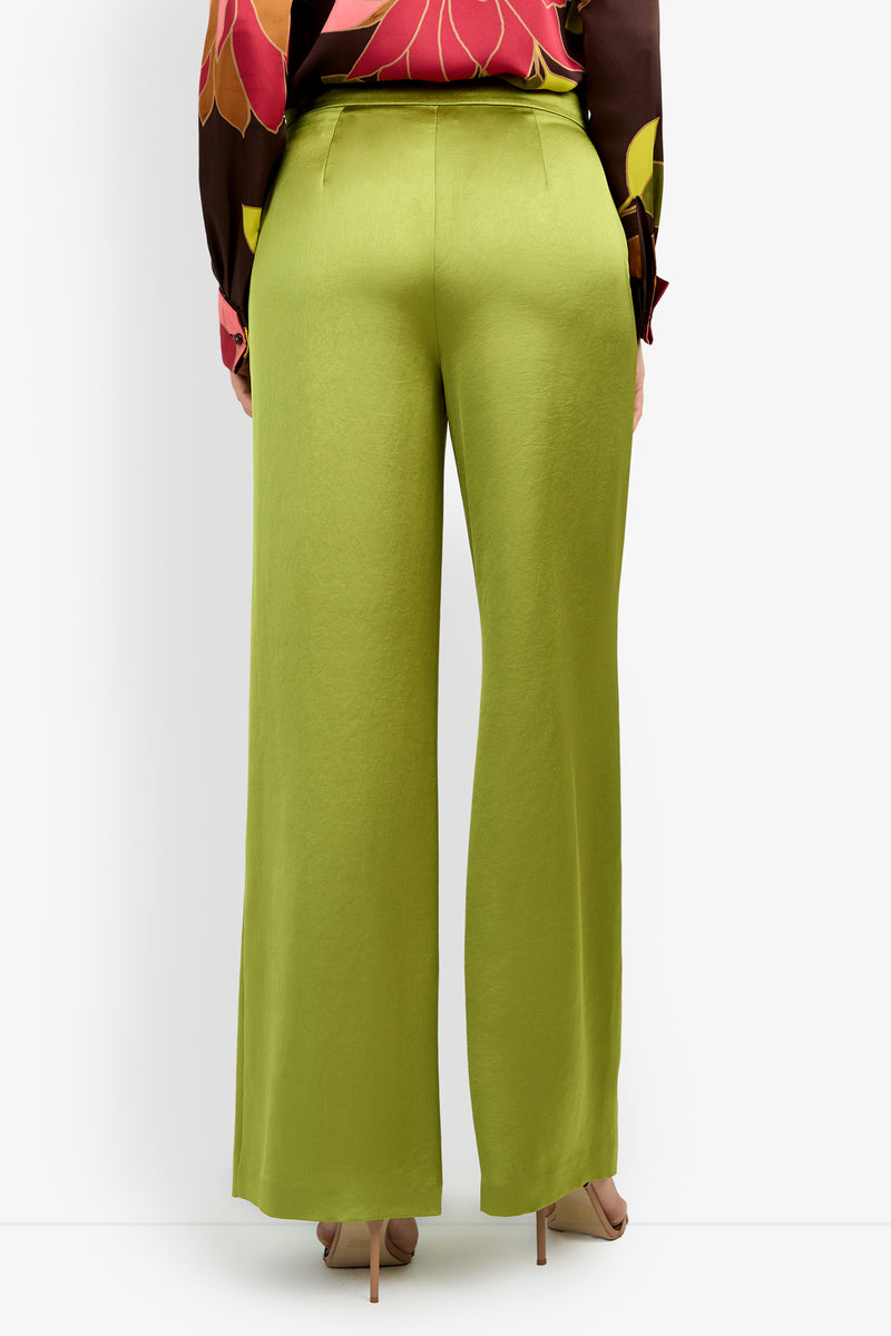 A person stands facing away, showcasing the back of the INES PANT in light green paired with a floral-patterned long-sleeve blouse and nude heels.