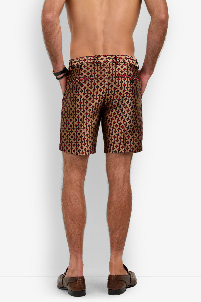 A man stands facing away, shirtless, wearing the Cataline Short—patterned in maroon, gold, and black—paired with brown loafers and black bracelets against a plain white background.