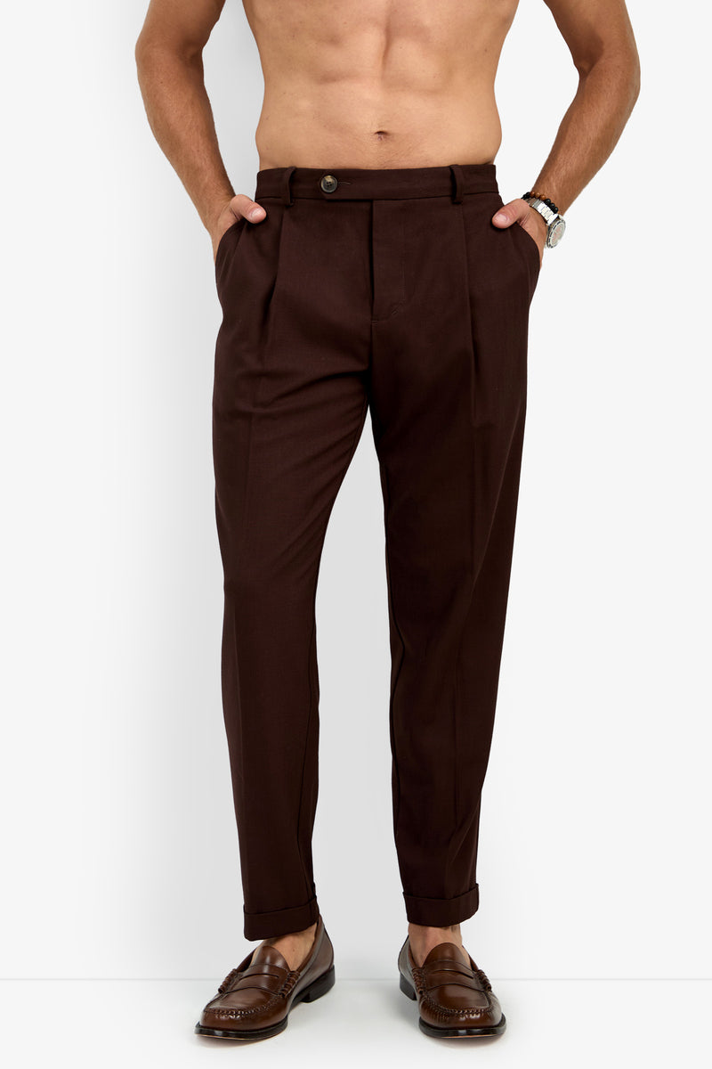 A shirtless man wearing the BEALE PLEATED TROUSER, paired with brown loafers and a wristwatch, stands with his hands in his pockets against a plain white background.