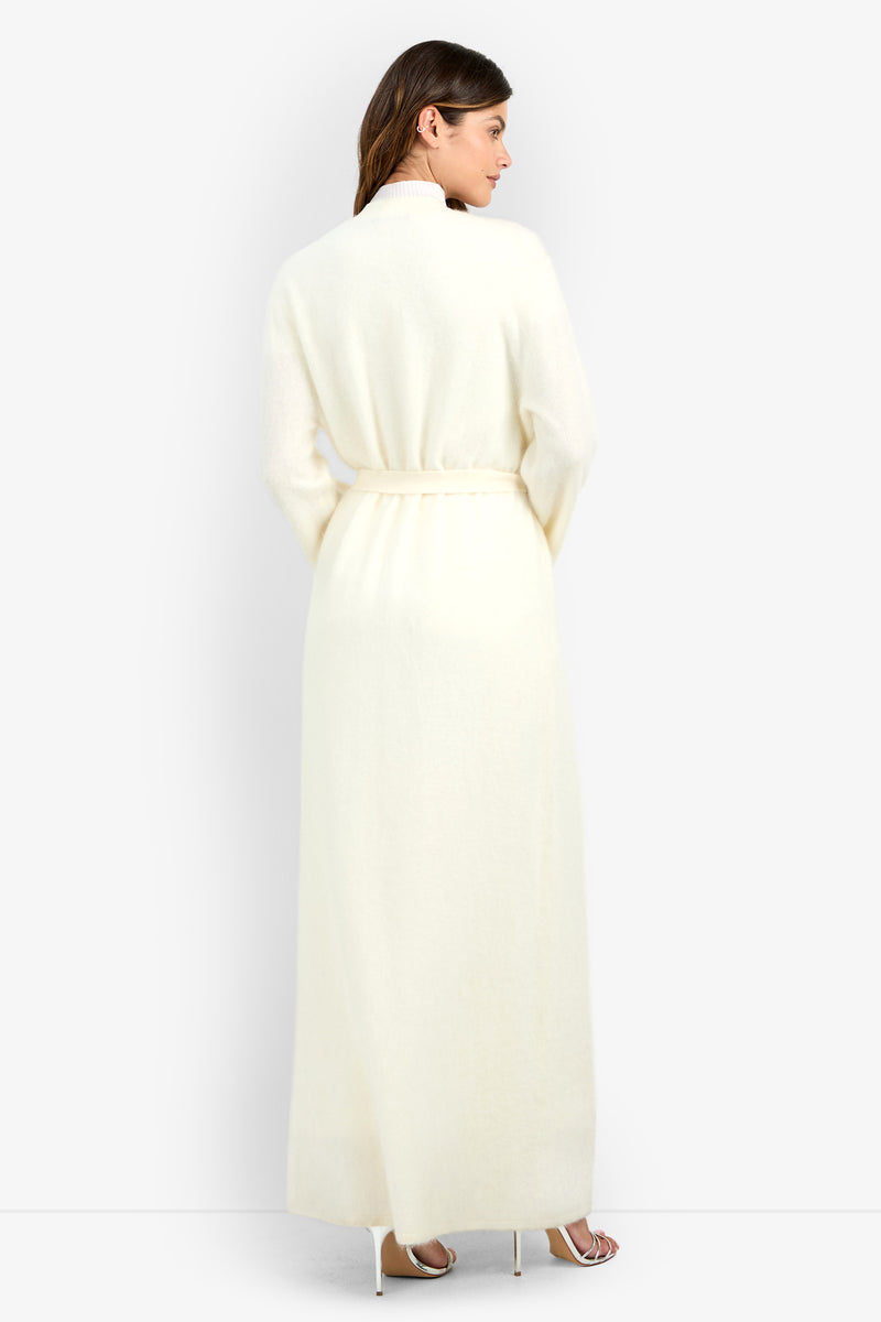 A woman viewed from behind wearing a floor-length, cream-colored belted Carducci Cardigan and heeled sandals.