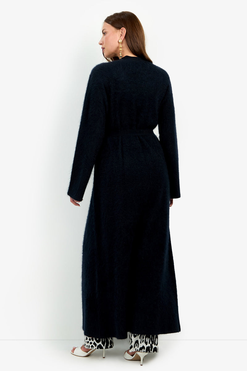 A person seen from behind wears a black, belted Carducci Cardigan over leopard-print pants and white heeled sandals.