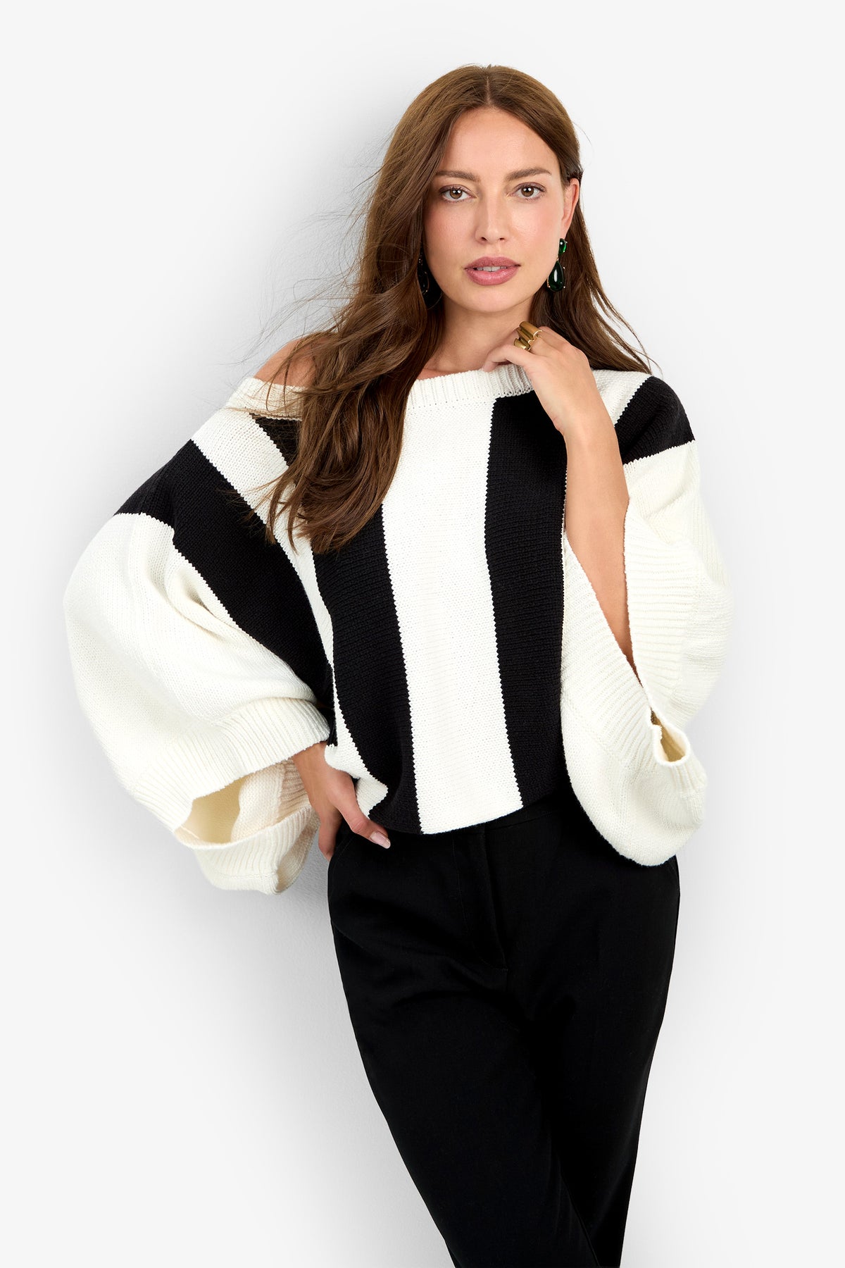 A person wearing a black and white vertically striped Horizon Sweater with an off-the-shoulder neckline, wide sleeves, and black trousers.