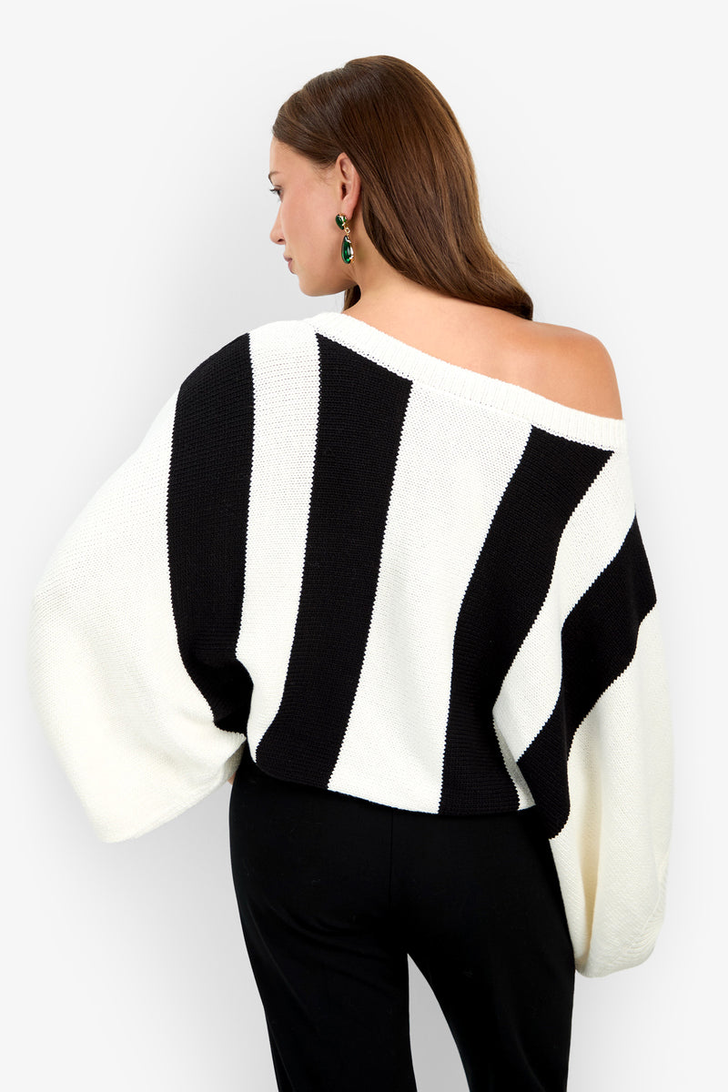 A woman seen from behind wearing an off-the-shoulder Horizon Sweater featuring black and white vertical stripes and wide sleeves.