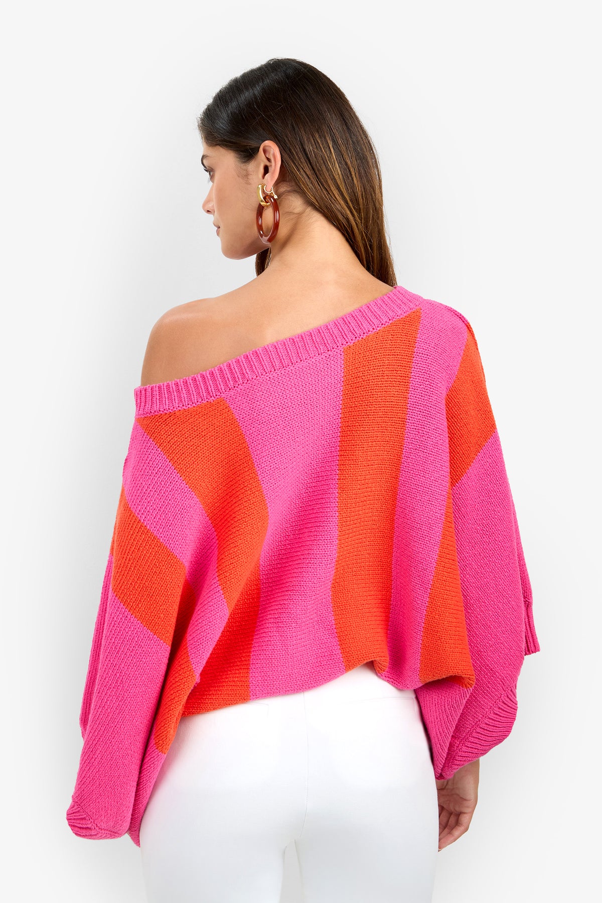 Back view of a person wearing an off-the-shoulder, oversized Horizon Sweater featuring thick pink and orange vertical stripes.