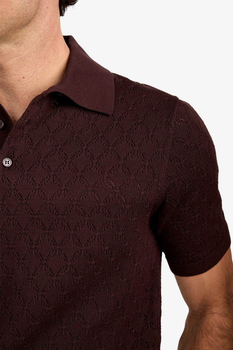 A close-up of a person wearing the Waylen Polo—a textured, dark brown short-sleeve shirt featuring a subtle diamond pattern. Only the shoulder, chest, and part of the face are visible.