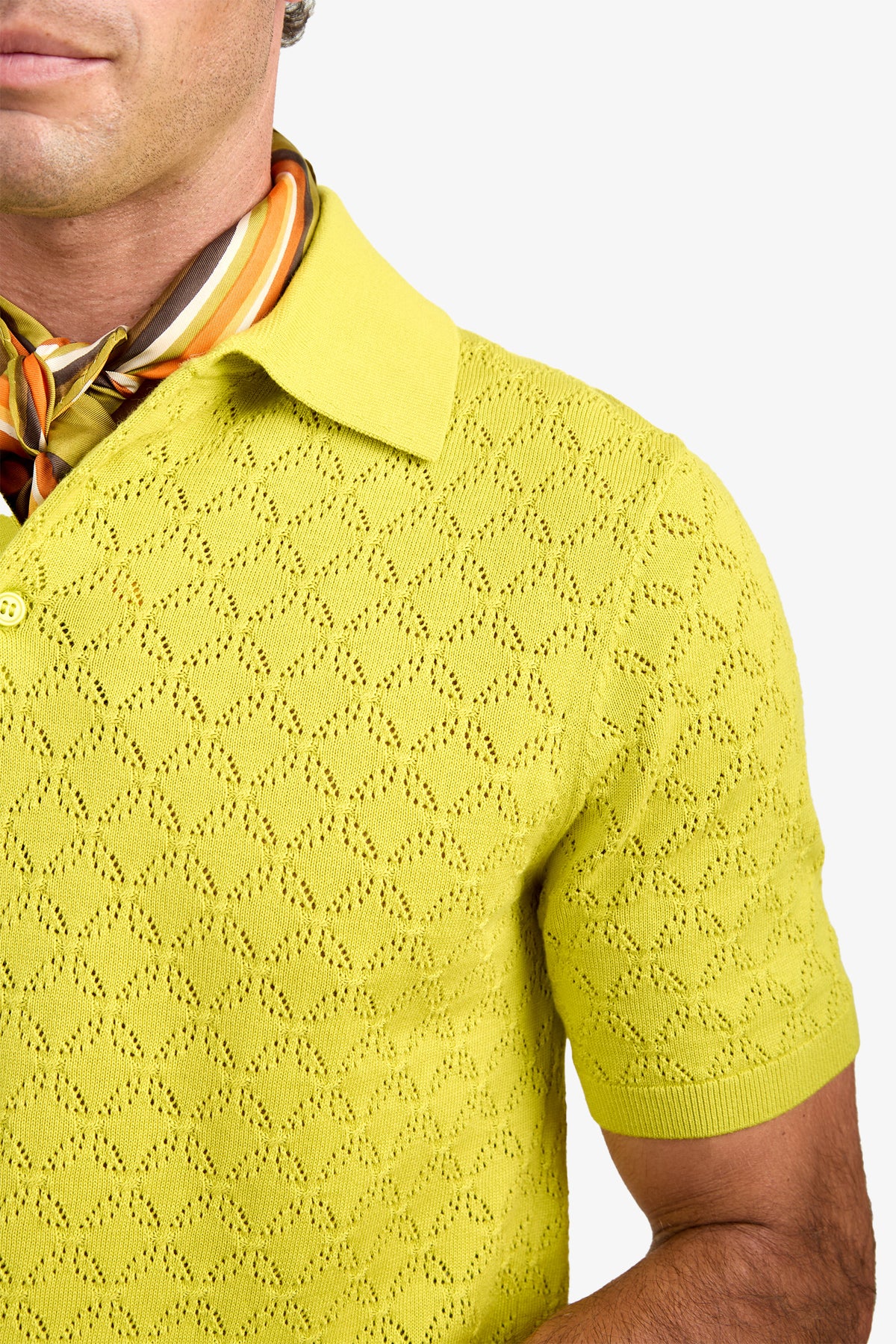 A person wearing the Waylen Polo, a textured yellow short-sleeve shirt, paired with a colorful striped scarf around their neck, shown from the shoulders up against a white background.