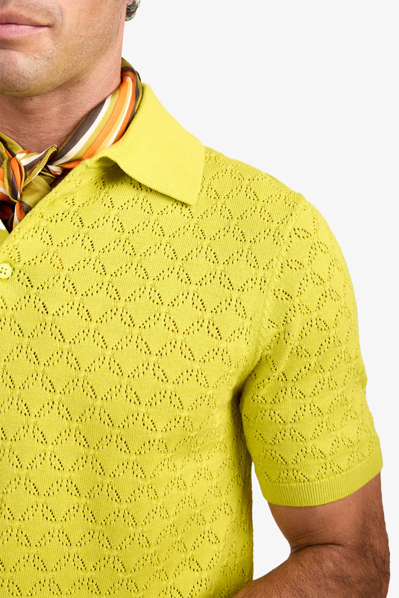 A person wearing the Waylen Polo, a textured yellow short-sleeve shirt, paired with a colorful striped scarf around their neck, shown from the shoulders up against a white background.