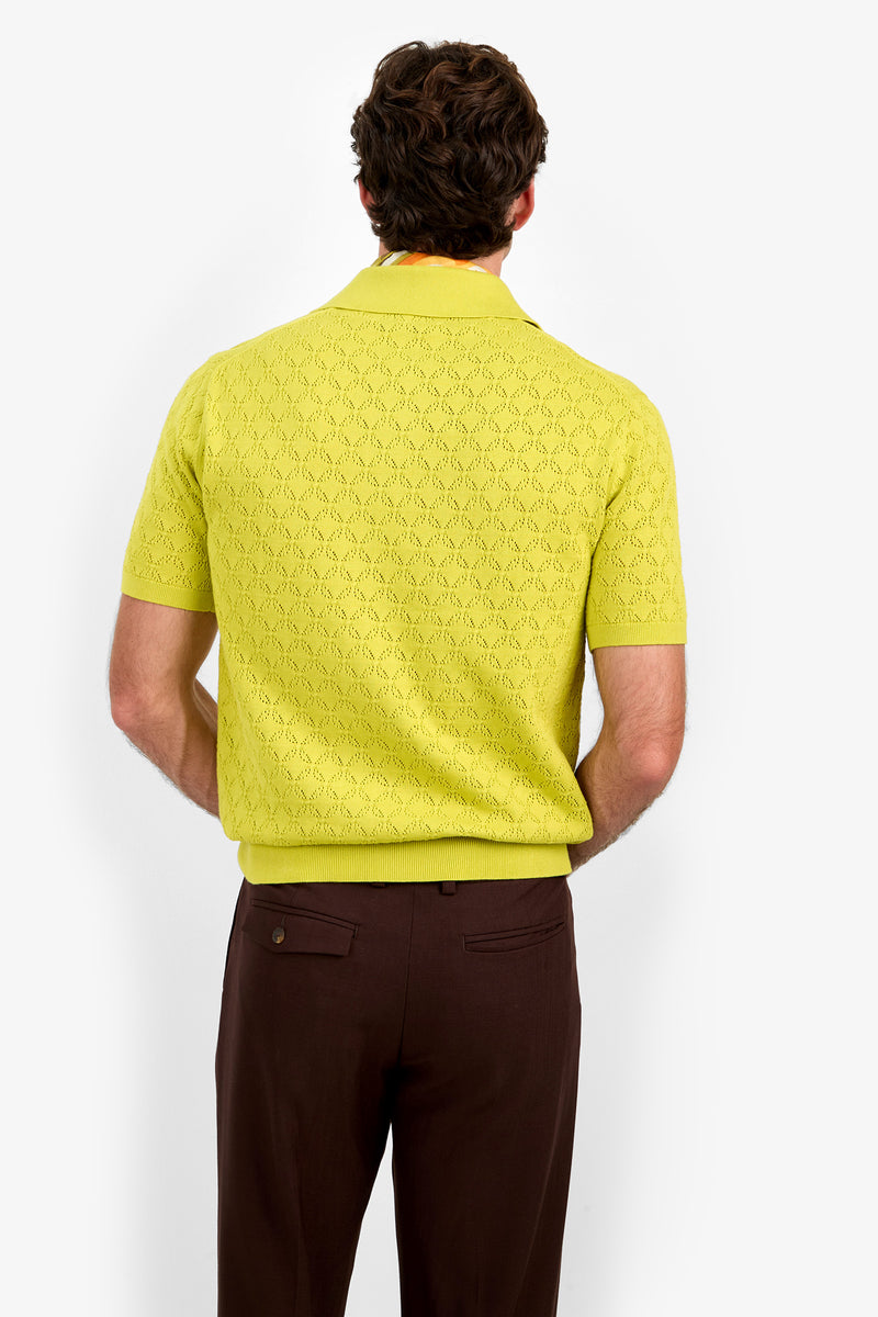A man stands facing away, wearing the short-sleeved yellow Waylen Polo and brown pants against a plain white background.