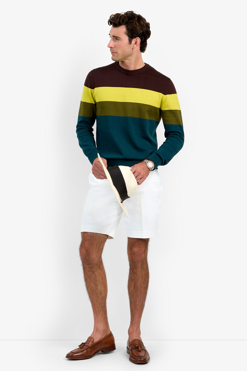 A man wearing the Roemer Crewneck, white shorts, brown loafers, and holding a hat stands against a plain white background, looking to the side.