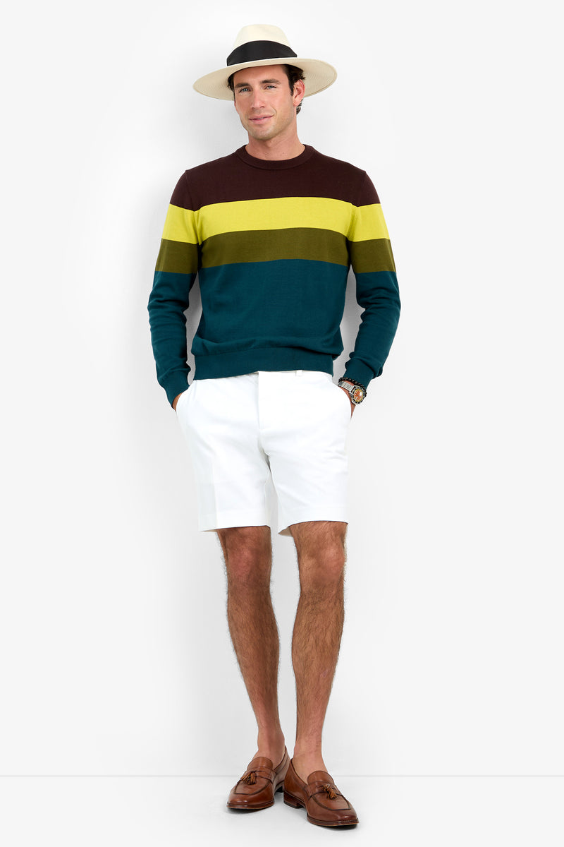 A man wearing the Roemer Crewneck, white shorts, brown loafers, and a white hat with a black band stands against a white background with his hands in his pockets.