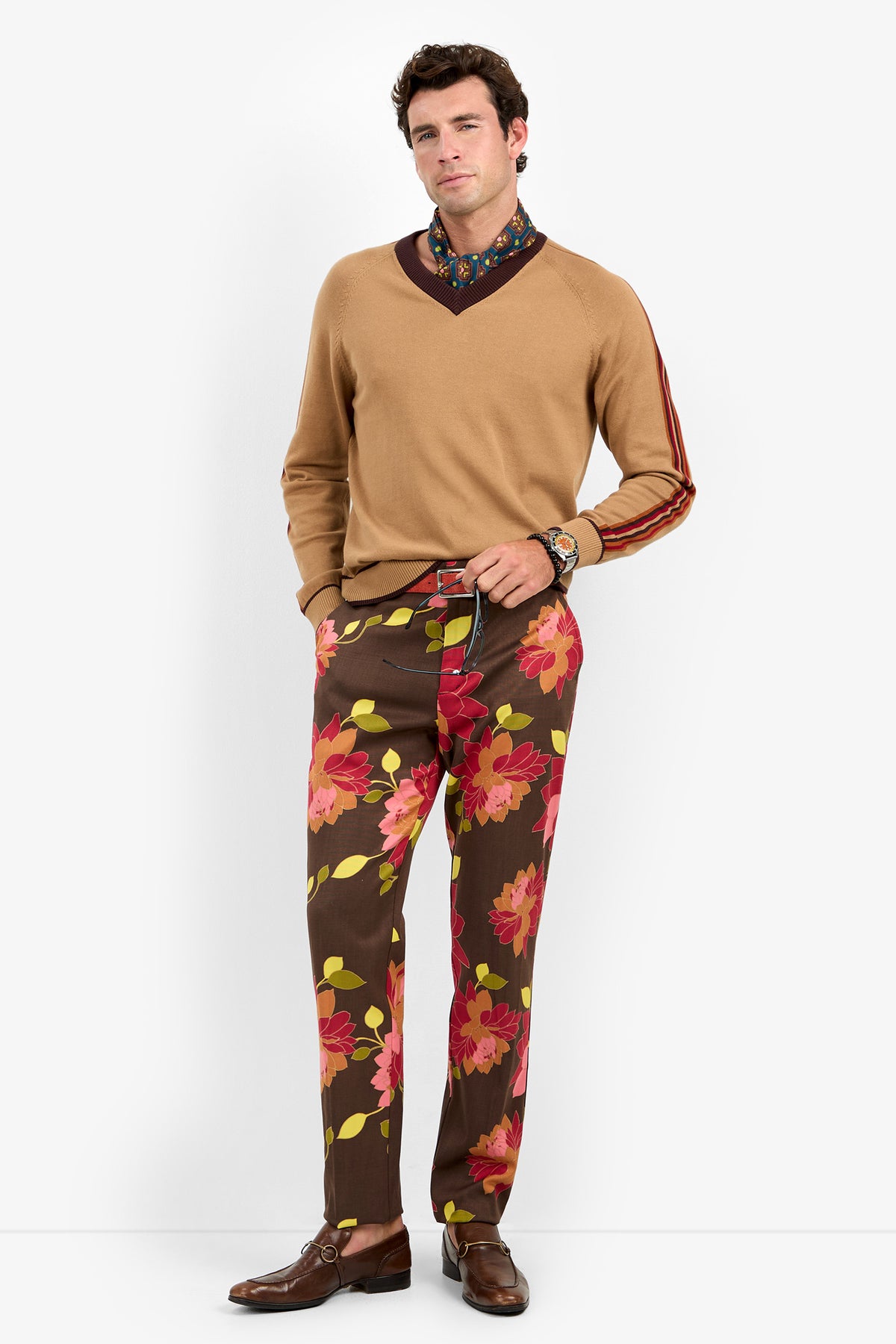 A man stands wearing the Harvey Sweater, paired with a patterned shirt and brown pants featuring large red and pink floral prints. He completes the look with brown dress shoes, a watch, and a confident expression against a plain white background.