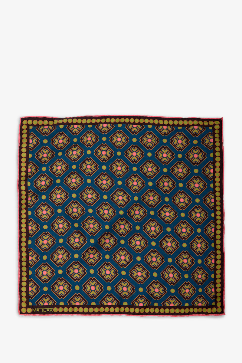The Pocket Square features a geometric pattern of blue, yellow, red, and pink shapes on a square fabric, framed by a row of gold circles and finished with a thin red border.