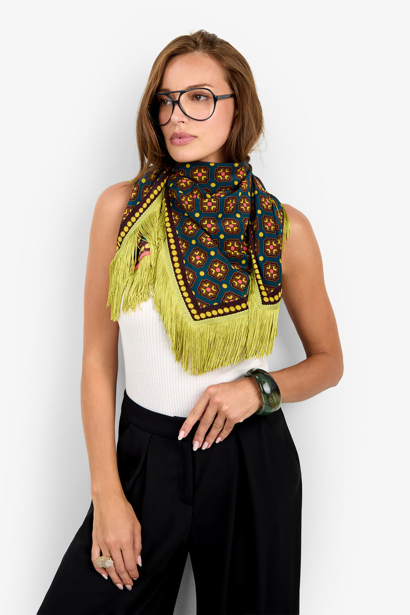A woman in glasses, a white sleeveless top, black pants, and the Foulard Scarf in Foulard stands against a white background.
