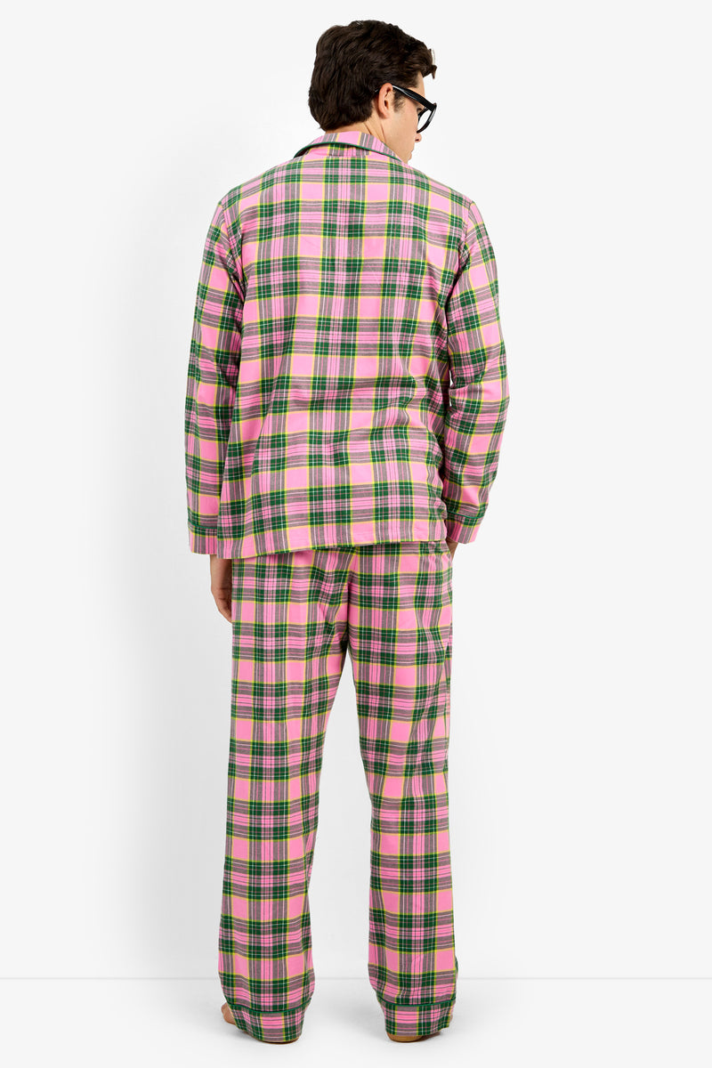 A man viewed from behind wearing a pink and green plaid pajama set with a matching long-sleeve top and pants, photographed against a plain white studio background.