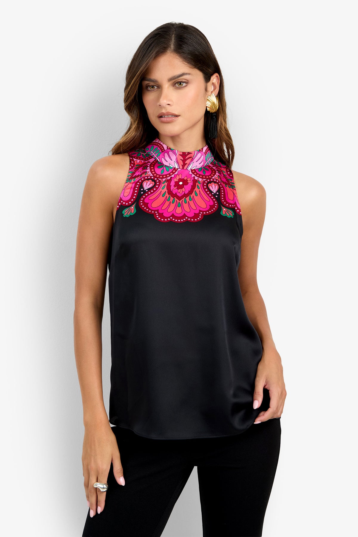A woman with long dark hair and gold earrings is shown wearing the Loveage Top—a sleeveless black design with a high neckline, adorned with vibrant pink and red embroidered floral patterns. She stands against a plain white background.
