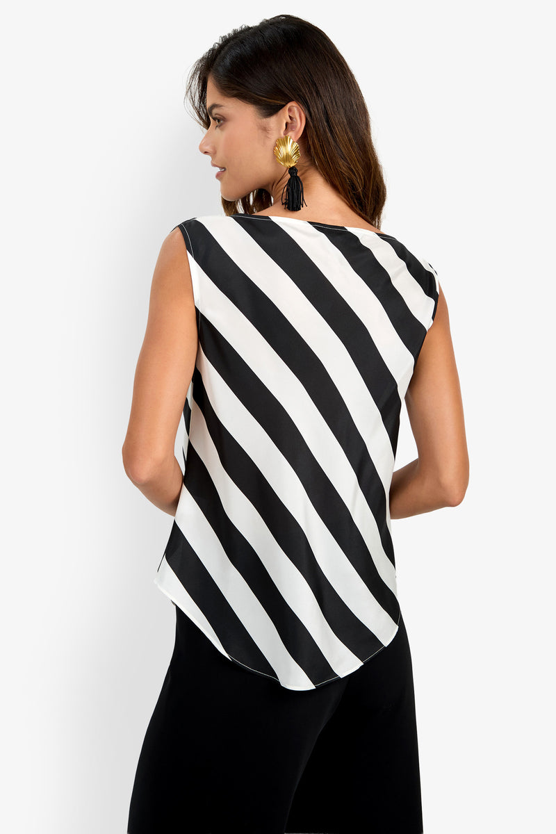 Woman wearing the Alessi Top—a sleeveless black and white diagonal striped design—paired with black pants and large statement earrings, facing away and looking to the side against a plain background.