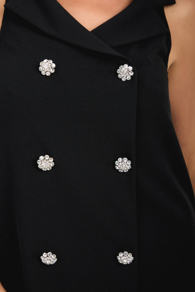 Close-up of the Siamo Dress, a black sleeveless garment featuring six decorative, flower-shaped silver and crystal buttons arranged in two vertical rows.