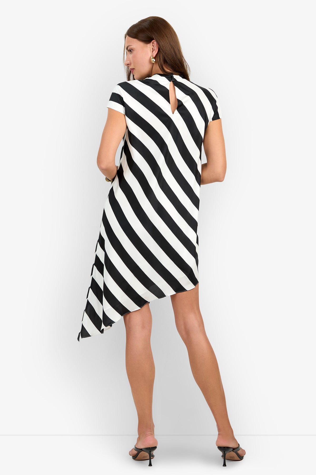 A person wearing the SHANA DRESS (1), a short-sleeve black and white diagonal striped asymmetrical dress, paired with black heels, stands with their back to the camera against a plain white background.