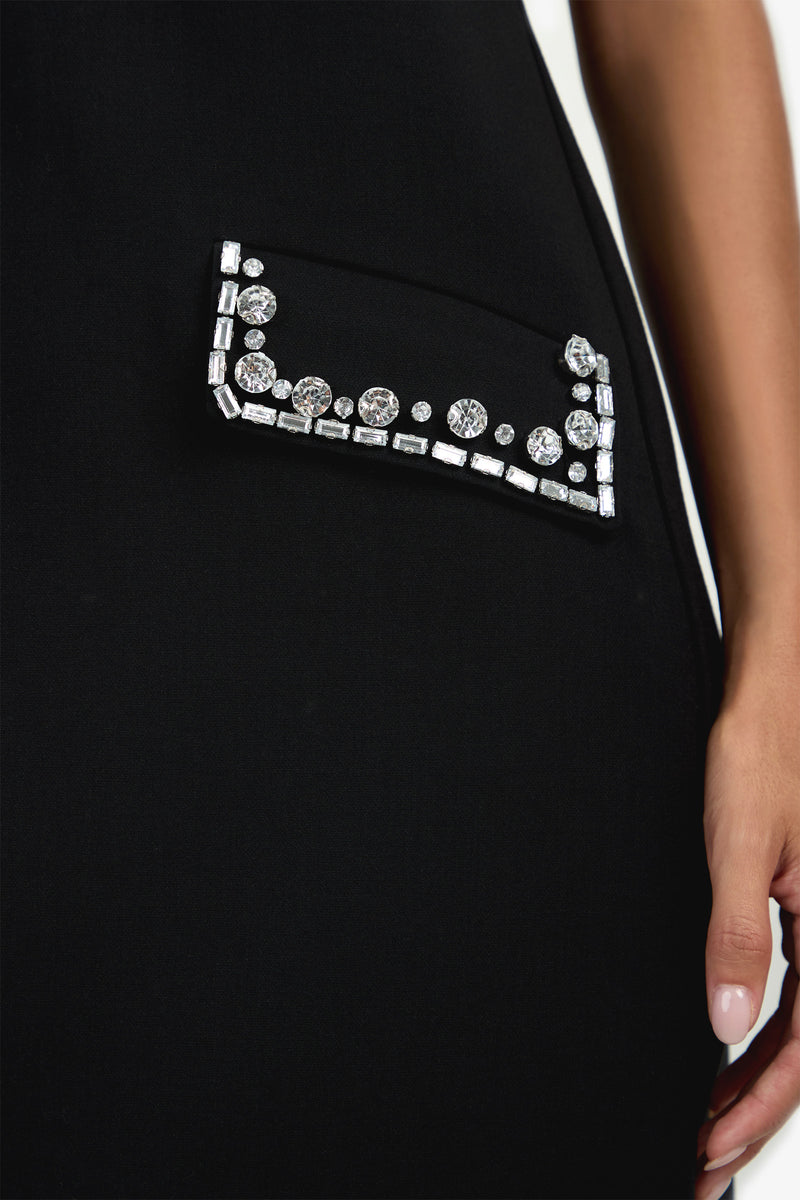 A close-up of the Sephine Dress shows a small embellished pocket adorned with shiny silver and crystal-like gems, next to a person’s hand.