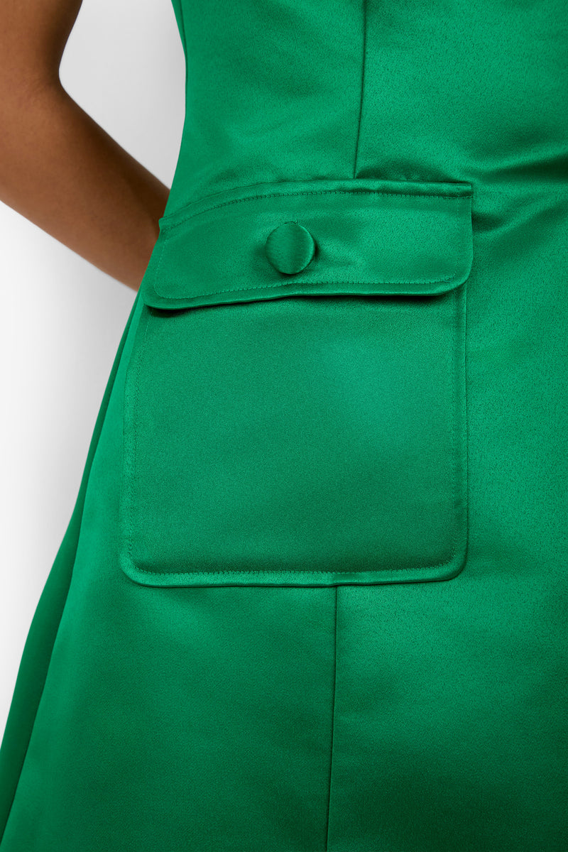 Close-up of the Guinevere Dress in green satin, showcasing a large pocket with a flap and a covered button. Only part of the wearer’s arm is visible on the left side of the image.