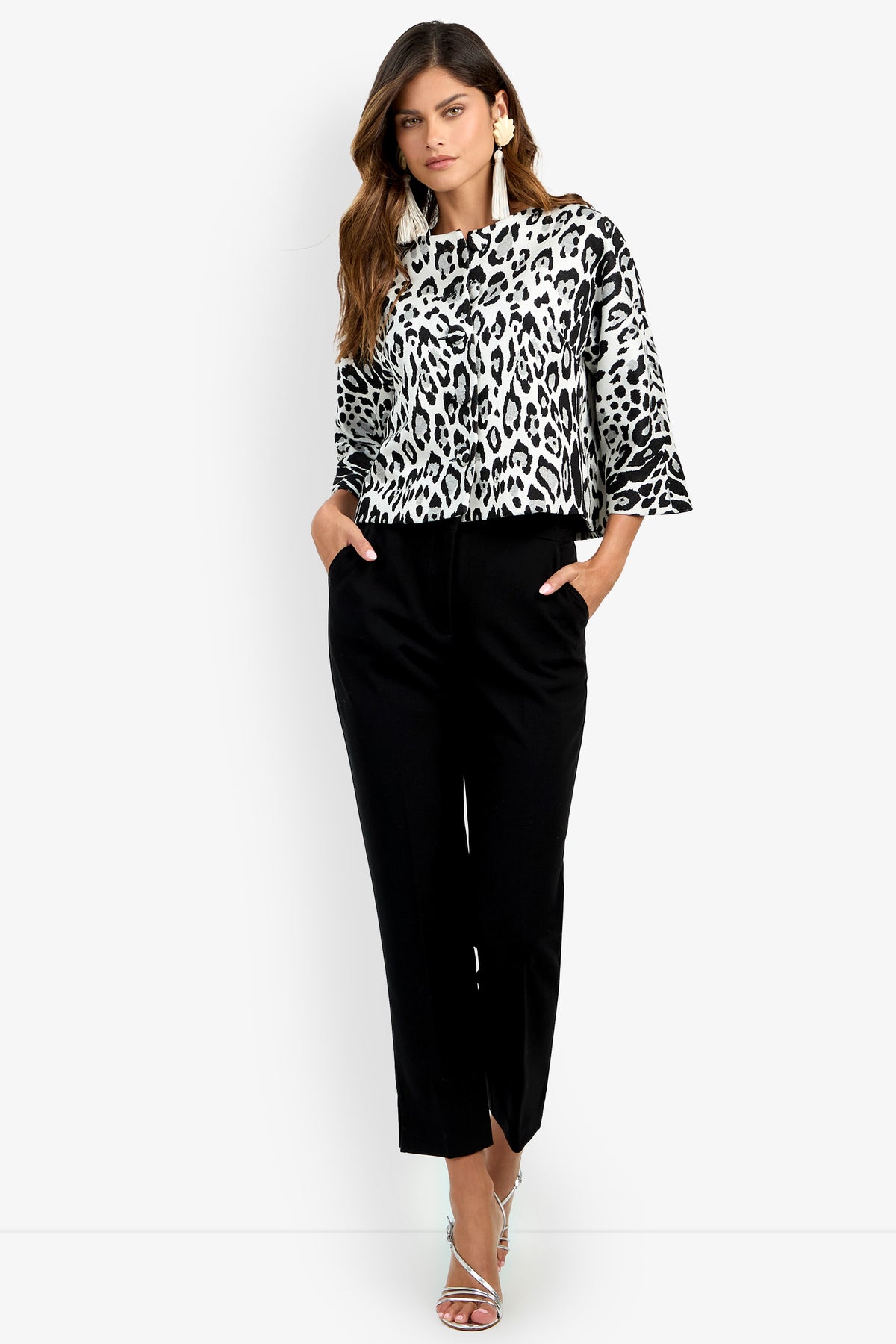 A woman wearing the Critique Jacket, featuring a black and white animal print, paired with black pants and silver heels, stands with her hands in her pockets against a white background.