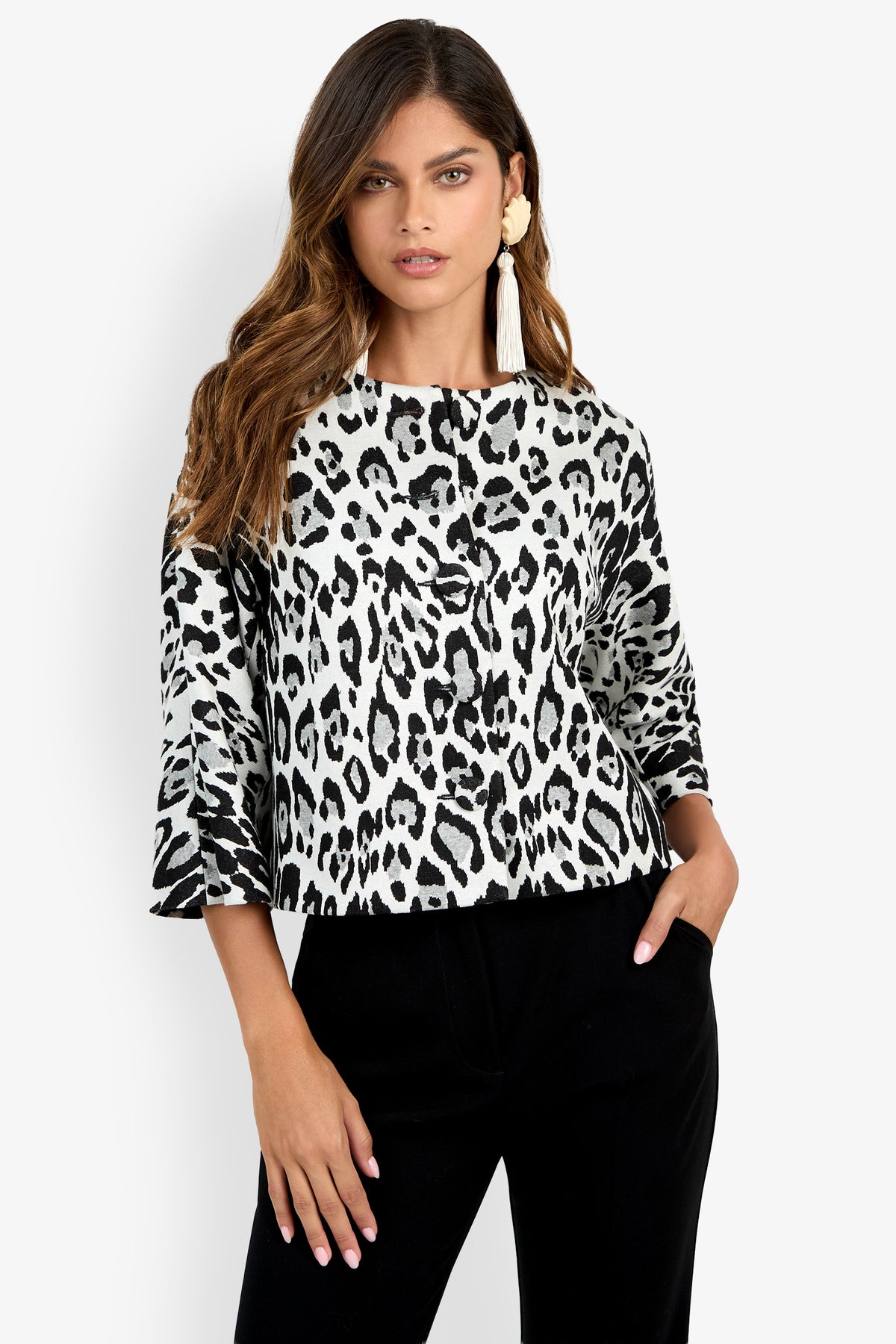 A woman wears the Critique Jacket—a black and white leopard print top with three-quarter sleeves—paired with black pants, posing with one hand in her pocket against a plain white background.