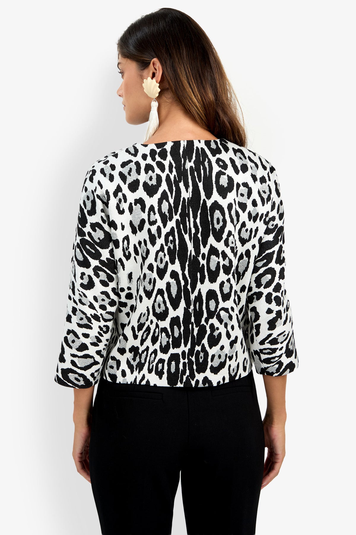 Woman facing away, wearing the Critique Jacket in a black-and-white animal print with three-quarter sleeves, paired with black pants and large white earrings.