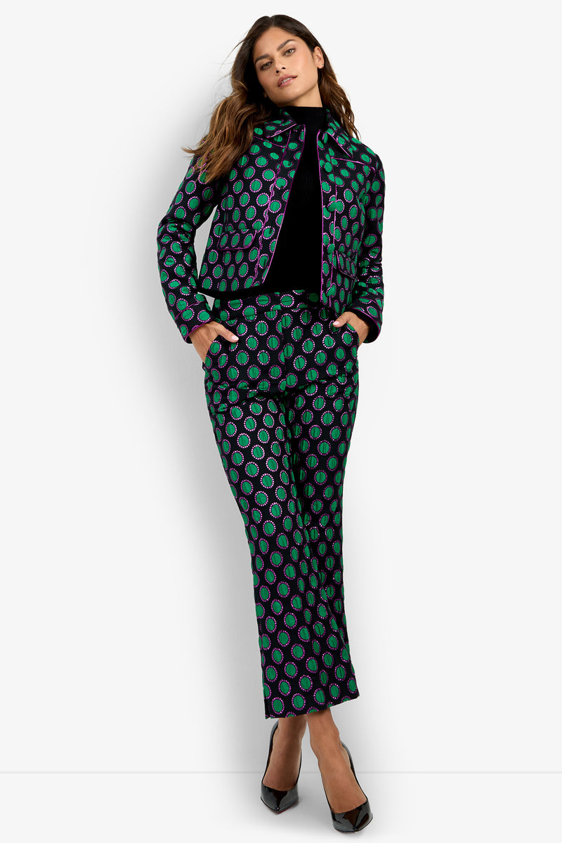 Model wearing the Allex Jacket in Gemstone with matching pants, hands in pockets, standing against a white background and looking confidently at the camera, styled with black heels.