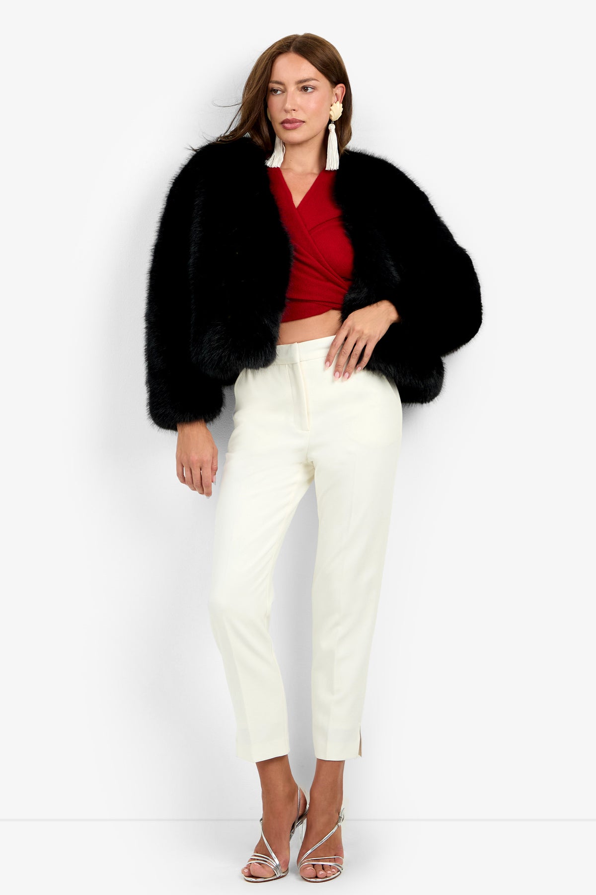 Woman wearing the Avenn Jacket in black, a red wrap top, white high-waisted pants, and silver high-heeled sandals, standing against a plain light background.