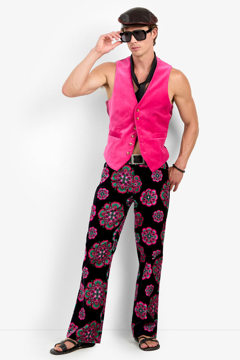 Man in the Irving Vest, black scarf, patterned bell-bottom pants, sandals, sunglasses, and a cap poses against a white background.
