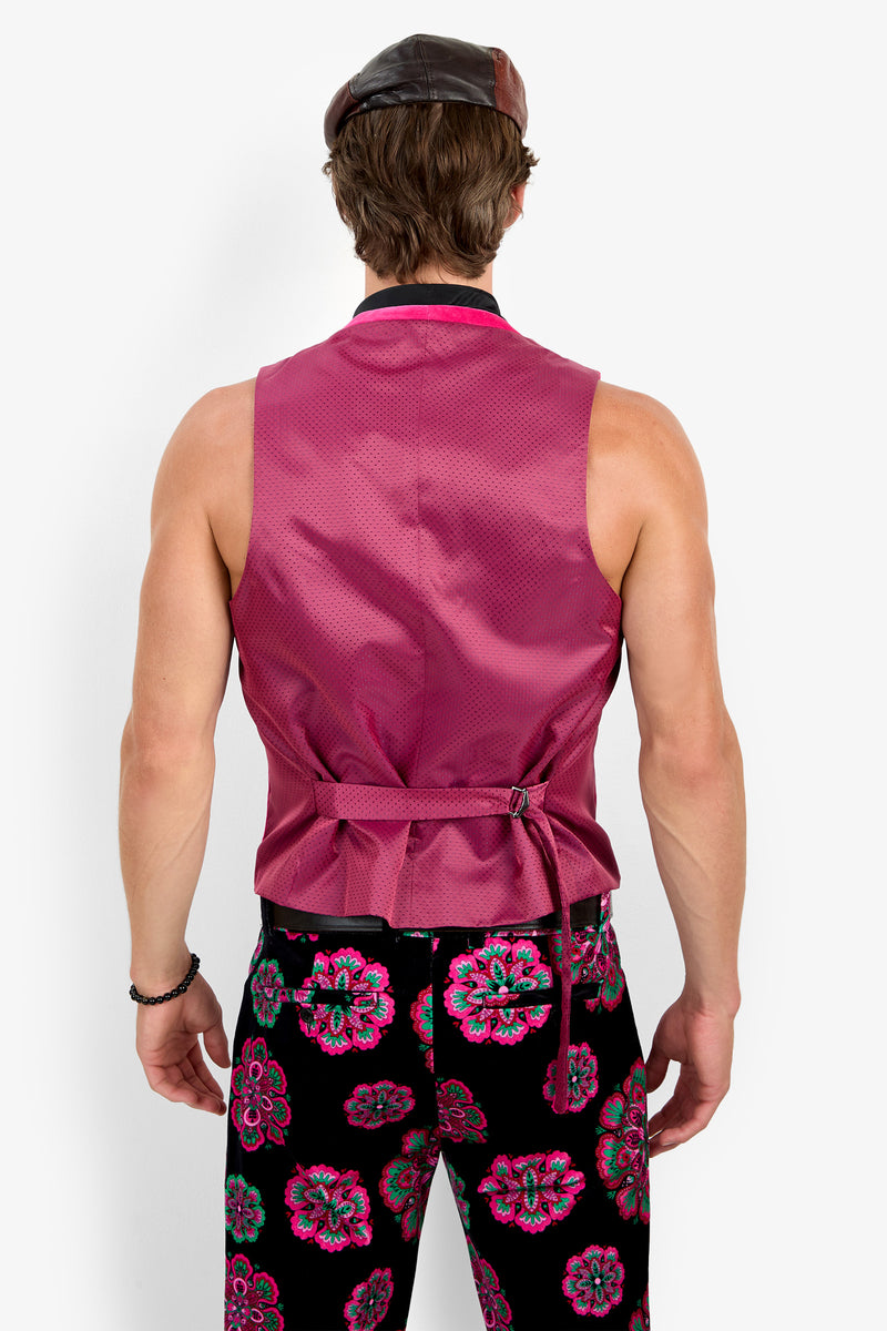 A man stands facing away, wearing the sleeveless magenta Irving Vest, a brown cap, and black pants with bright pink and blue floral patterns.